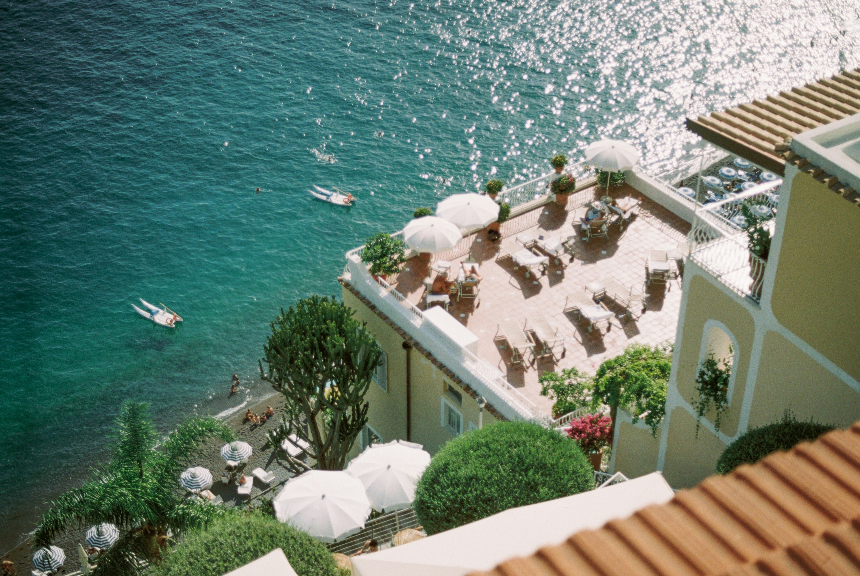 Aerial view of a sunlit Mediterranean clifftop terrace overlooking turquoise sea